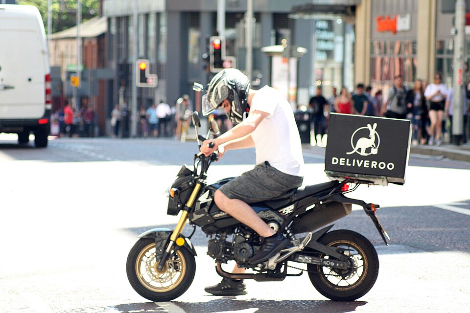 A Deliveroo motorbike delivery driver in Manchester on a sunny day.