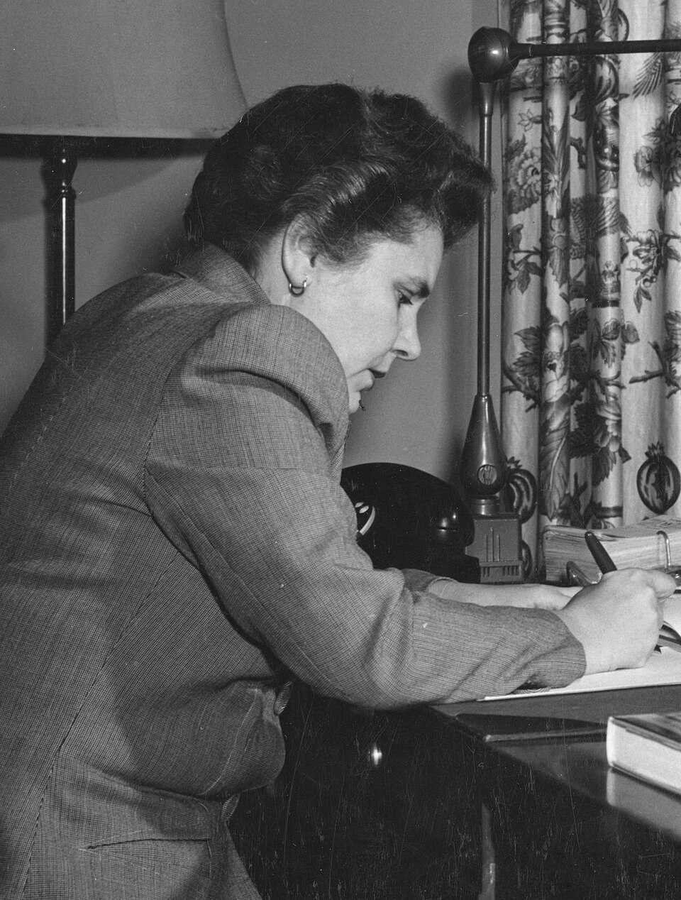 Elizabeth Bishop writing at her desk in the Library’s Poetry Office, with the U.S. Capitol in the background, circa 1949-1950.