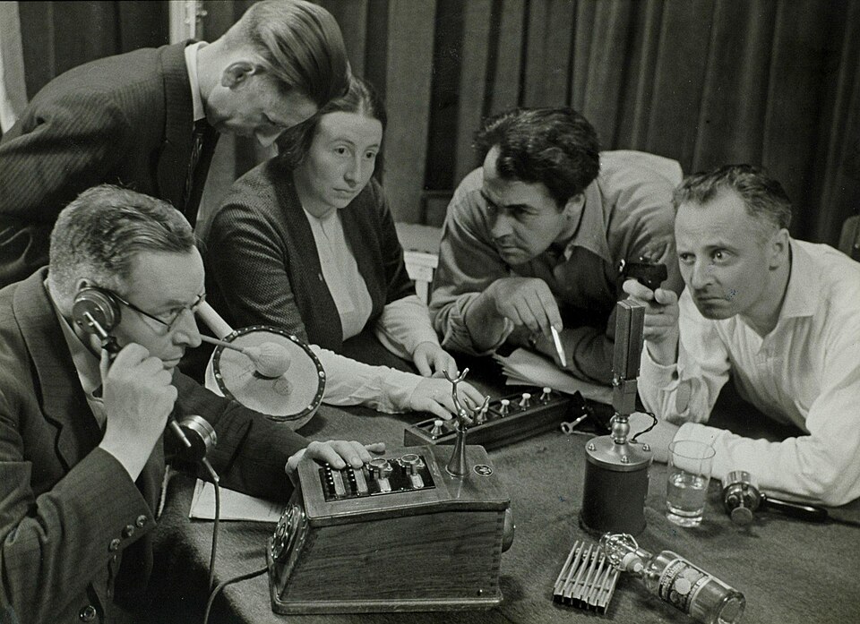 Recording a radio play. The Netherlands, 1949. The devices on the table, including the prop gun at right, are used to produce live sound effects during the…